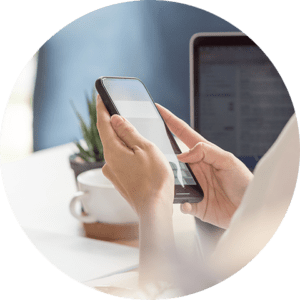 hands holding a smartphone with a laptop in the background