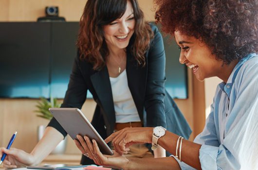 Two business women with a tablet smiling