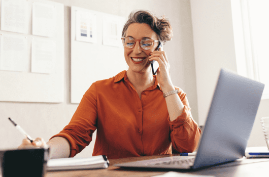 business woman holding a phone in front of a computer screen